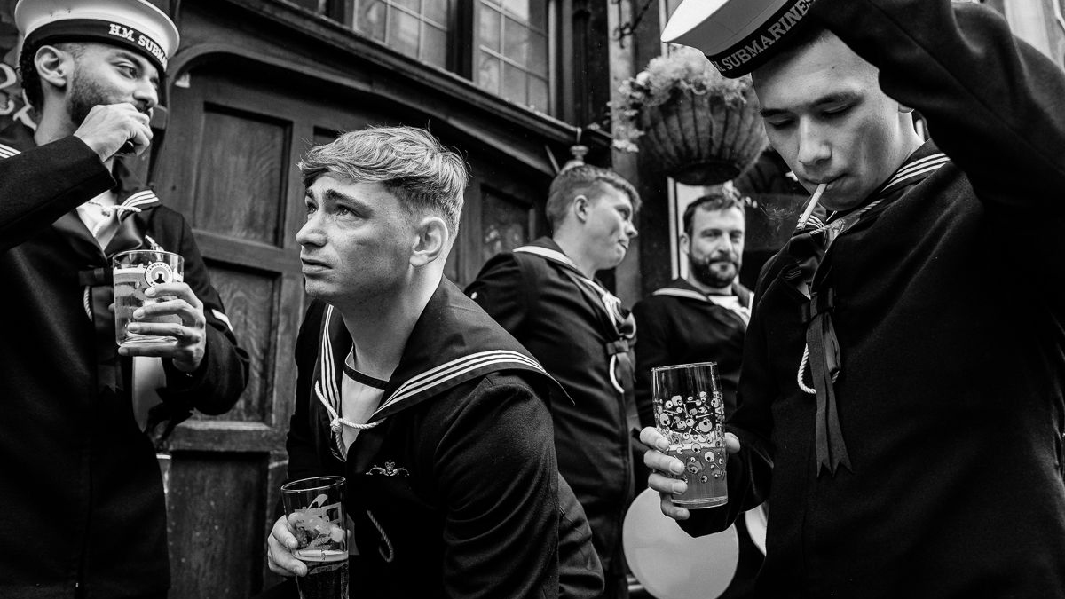 Black-and-white photo of five sailors in uniform drinking and smoking outside a building
