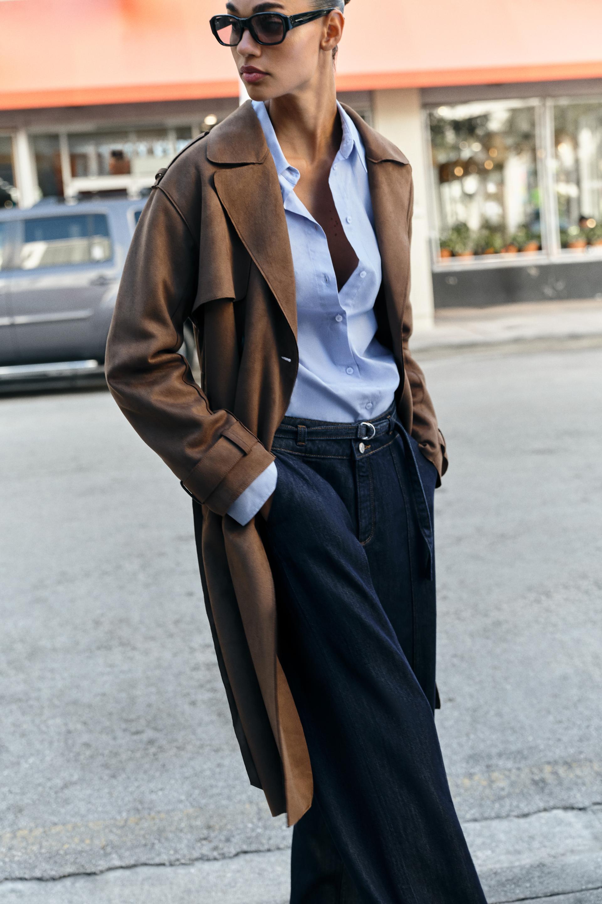 Model wears suede trench coat, blue shirt, blue jeans