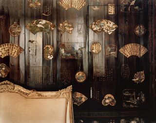 Room in Coco Chanels apartment, light gold headboard, brown dark wooden walls with gold detail, dark wooden door in the backdrop