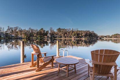 Two Adirondack chairs on a dock looking over a lake.