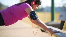 Woman wearing headphones and activewear, doing press up on a bench, highlighting the benefits of 1 minute of exercise per day