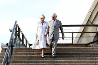 Queen Camilla wears a white dress and King Charles wears a gray suit and sunglasses in Sydney on the Opera House steps