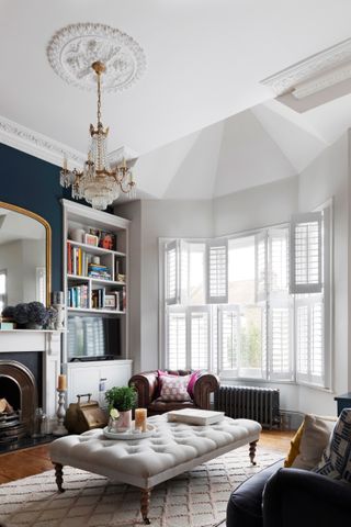 A large living room with central off-white ottoman with quilting detail