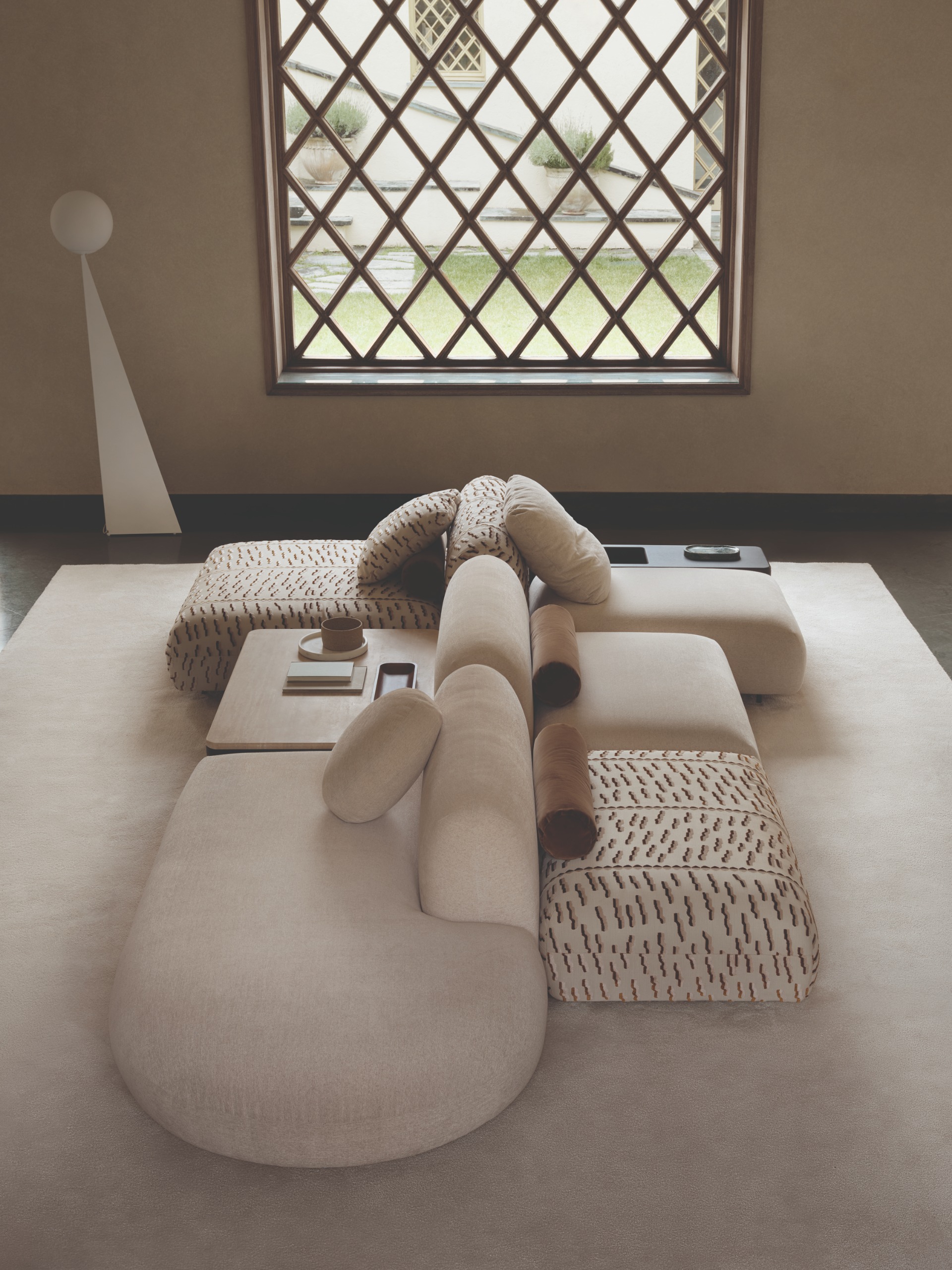 A modular sofa in cream and patterned in sections with velvet bolsters in front of a large framed window