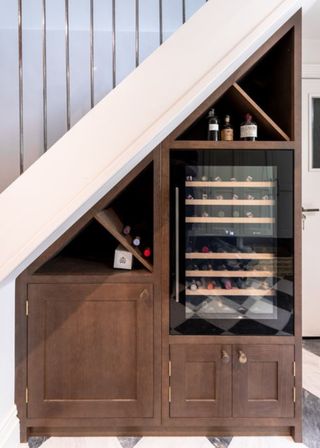 A wine cooler under the stairs with extra storage in wooden cabinets.