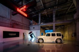 A white Mercedes-Benz in an industrial space with an overhead neon sign saying "DESIGN"