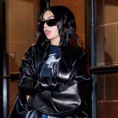 Charlie xcx wearing a black leather jacket, blue jeans, and black boots