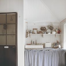 A rustic-style wall-panelled kitchen painted in white with a striped blue curtain covering the under-sink area