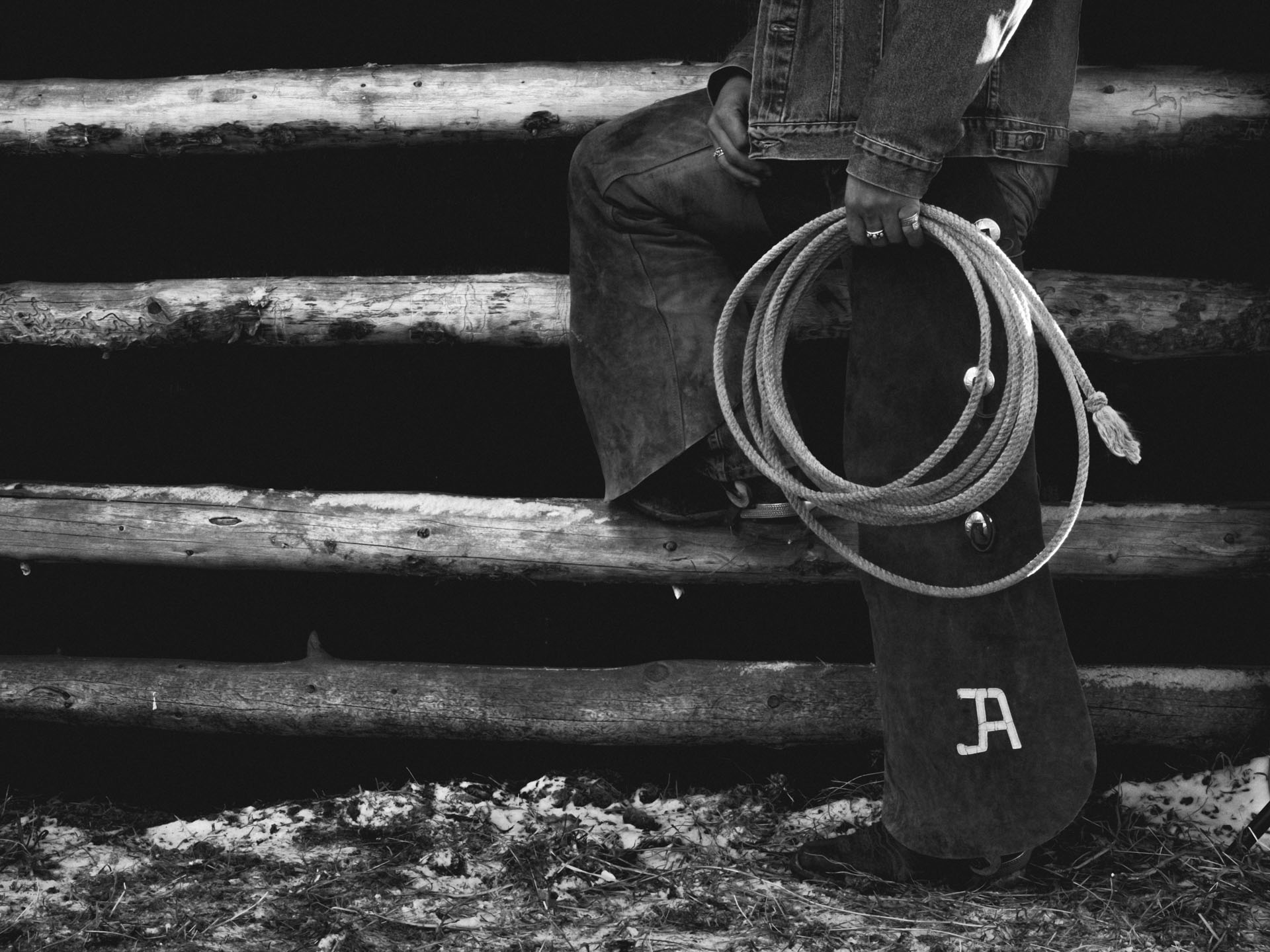 Black and white image of a cowboy model's legs, they are holding onto a rope