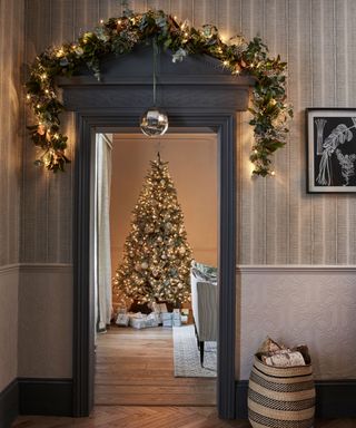 Doorway decorated with garland, christmas tree in background