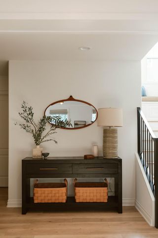 A light entryway with dark wood console table, hanging mirror, lamp and house plan