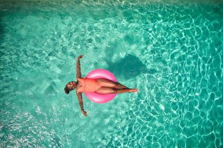 A woman lying in a bright pink doughnut float on a blue swimming pool.