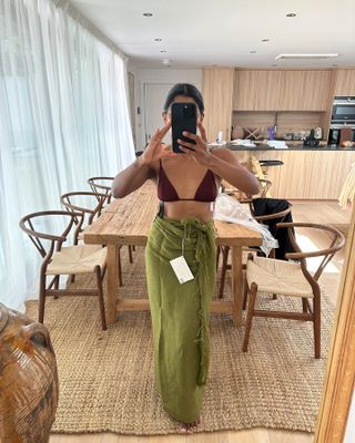 Woman in mirror wears brown triangle bikini top and green sarong