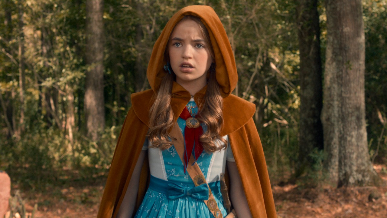 Holly in a blue dress with a yellow cape. Her hood is on.