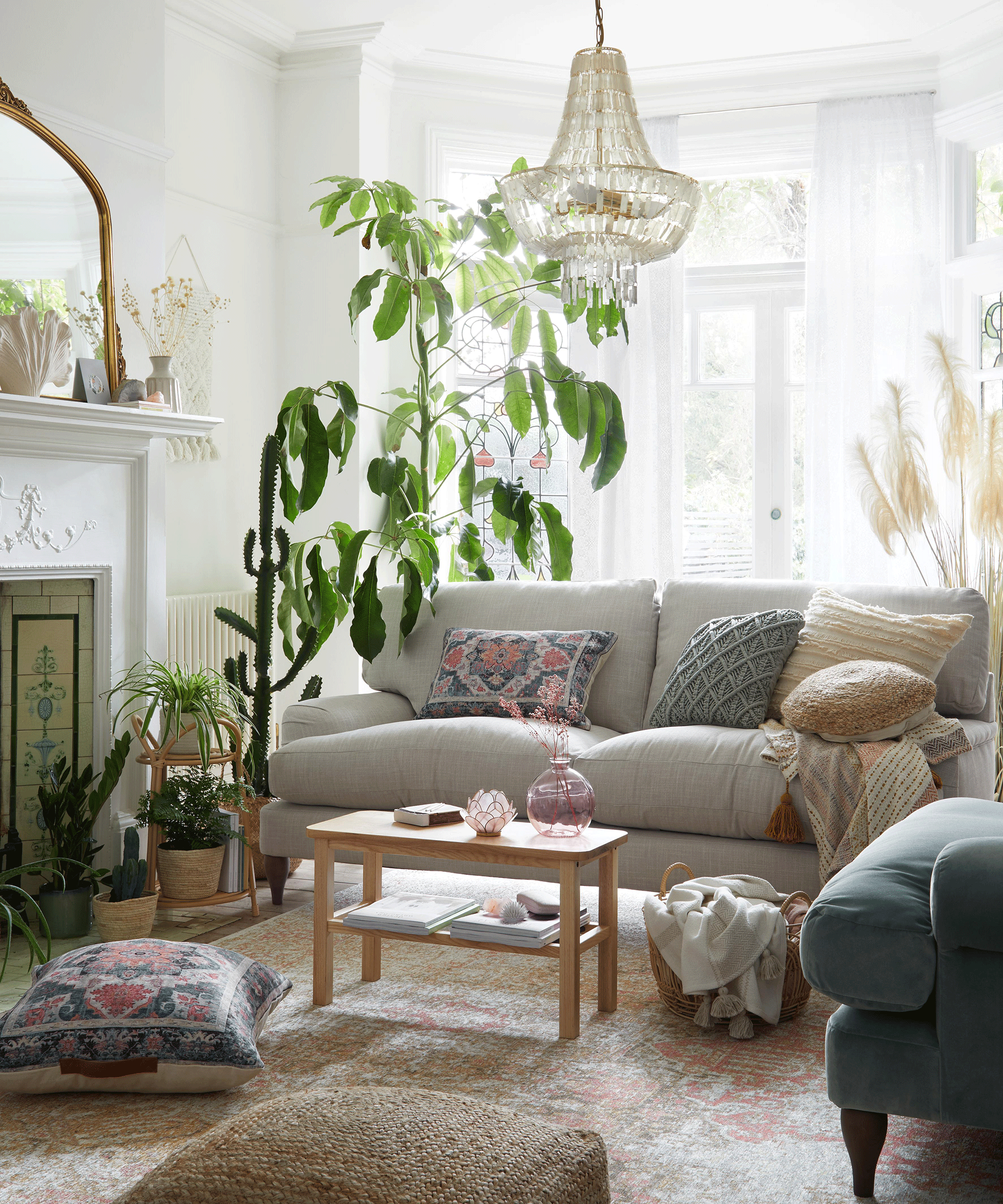 A modern bohemian living room with grey slubby sofa, traditional floor rug, indoor houseplants and textured cushions
