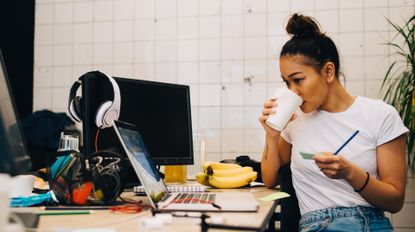 Woman drinking a cup of coffee and working at a desk with a computer