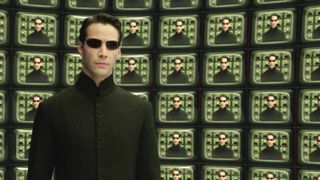 The Matrix movies, ranked - A still from The Matric Reloaded (2003). Neo (slicked back hair, black sunglasses, and a long black trench coat) standing in front of dozens of TV screens, all displaying him.