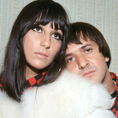 Cher wears a white fur coat while ex-husband Sonny Bono stands behind her wearing a black and red checked shirt in 1966