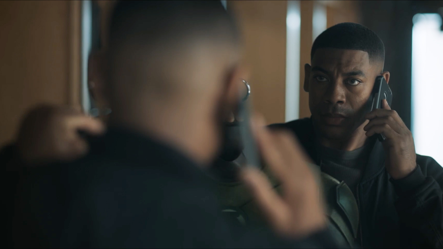 John Stewart on the phone and looking into a mirror while holding up a Green Lantern suit in Lanterns episode 2