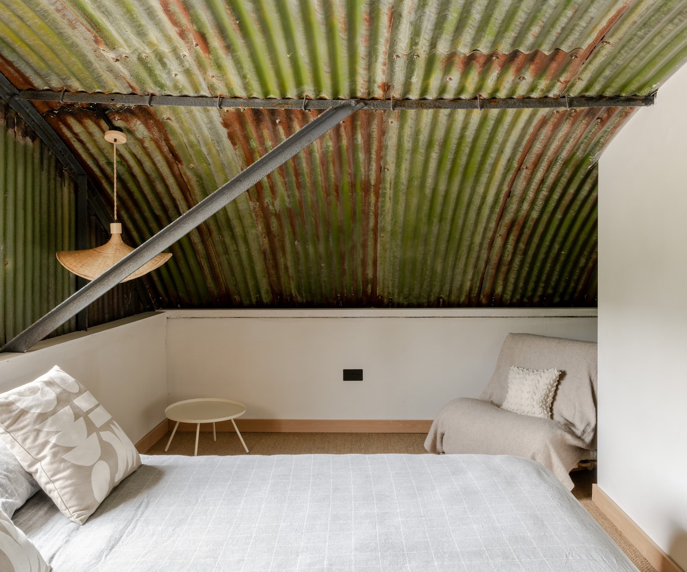 A white bed underneath a steel Corten roof