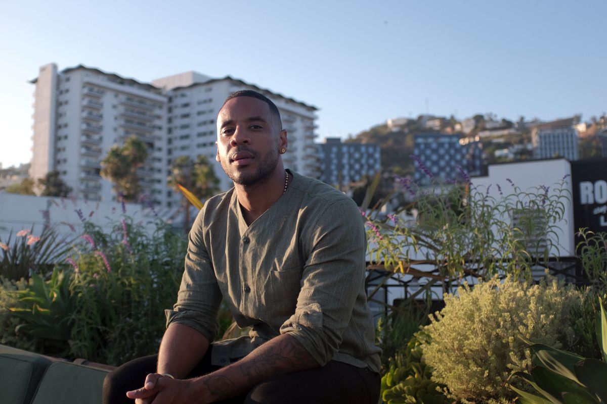 Reggie Yates sitting on a wall