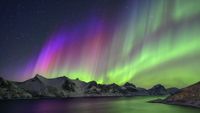 Green and purple auroras over snowy mountains and a lake