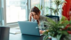 A bored looking businesswoman stares at her laptop, with her hand against her head.