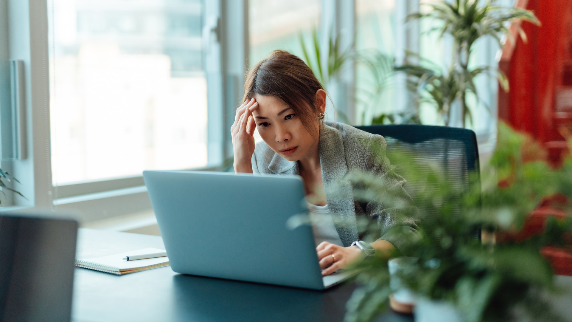 A bored looking businesswoman stares at her laptop, with her hand against her head.