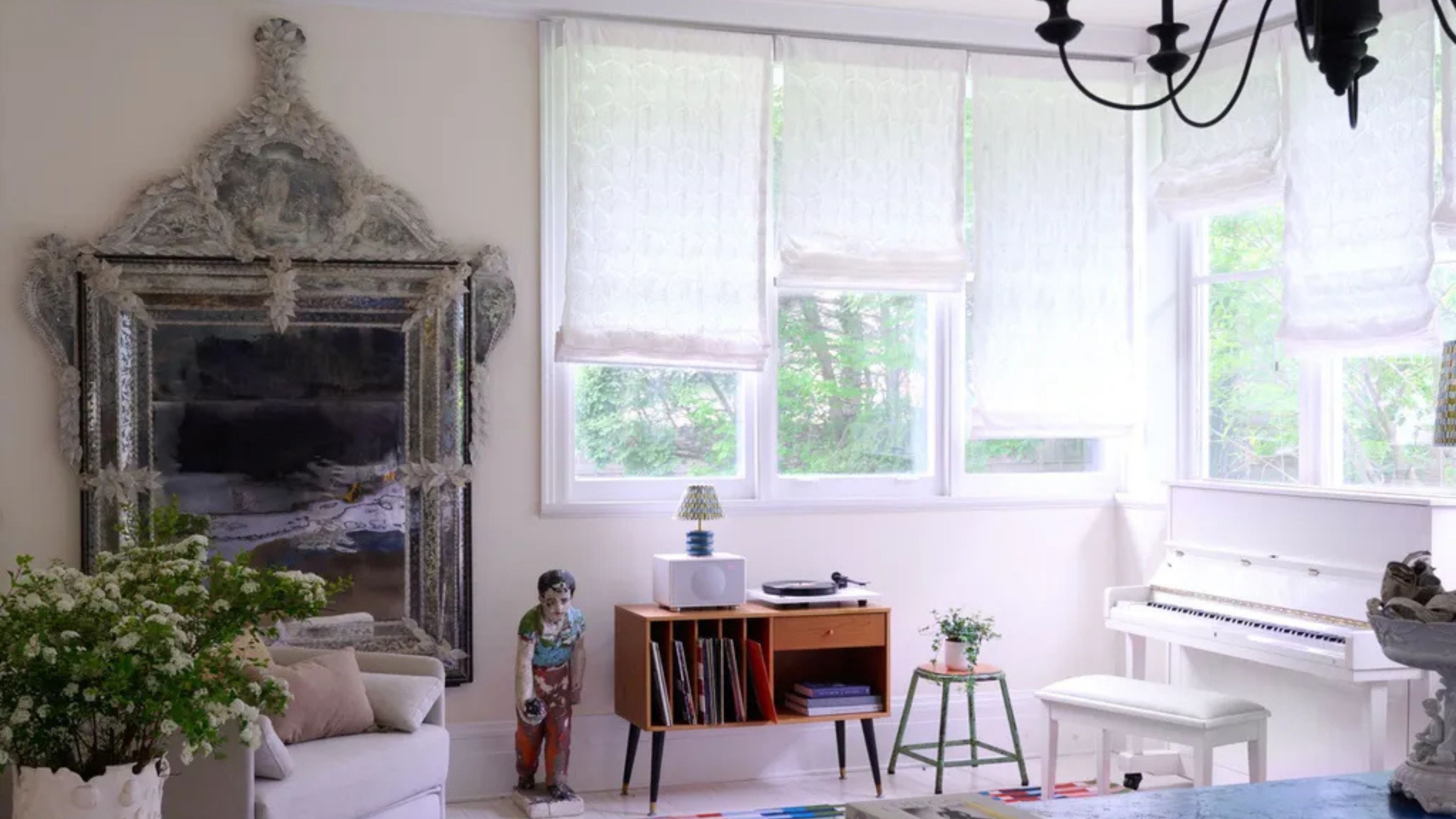 Pale pink living room with large vintage mirror, large windows with white drapes and quirky furniture