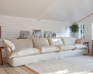 A large off-white sofa with loose cushions on a rustic wooden floor