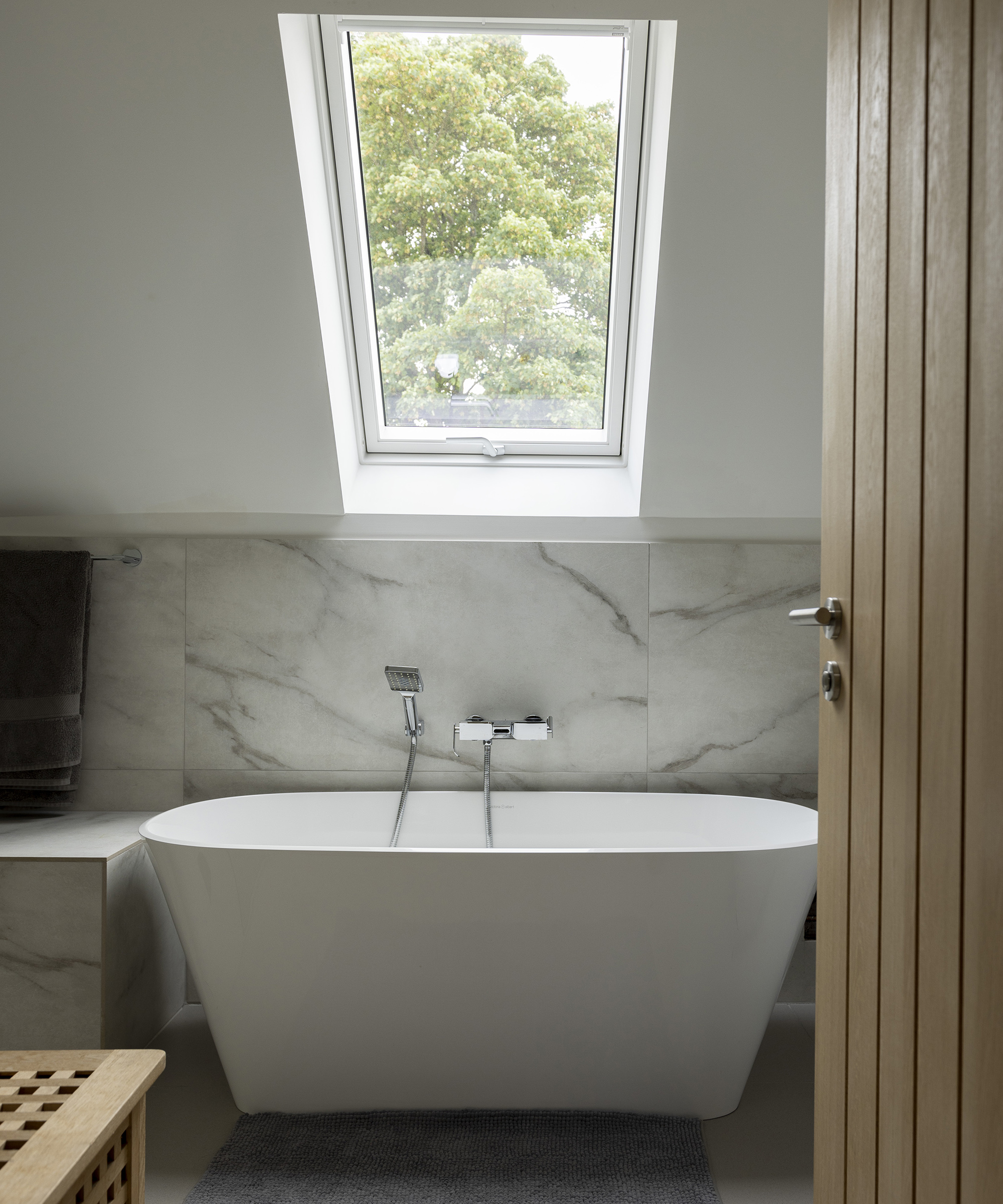 A free standing contemporary bath tub with marble style panelling and rooflight