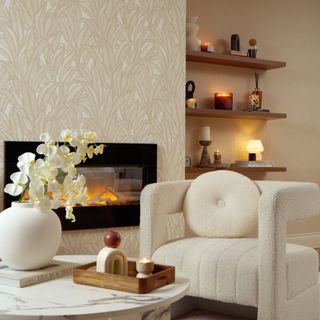 I Love Wallpaper Riviera Tropical Wallpaper in Cream in a living room with an electric fireplace and a boucle chair