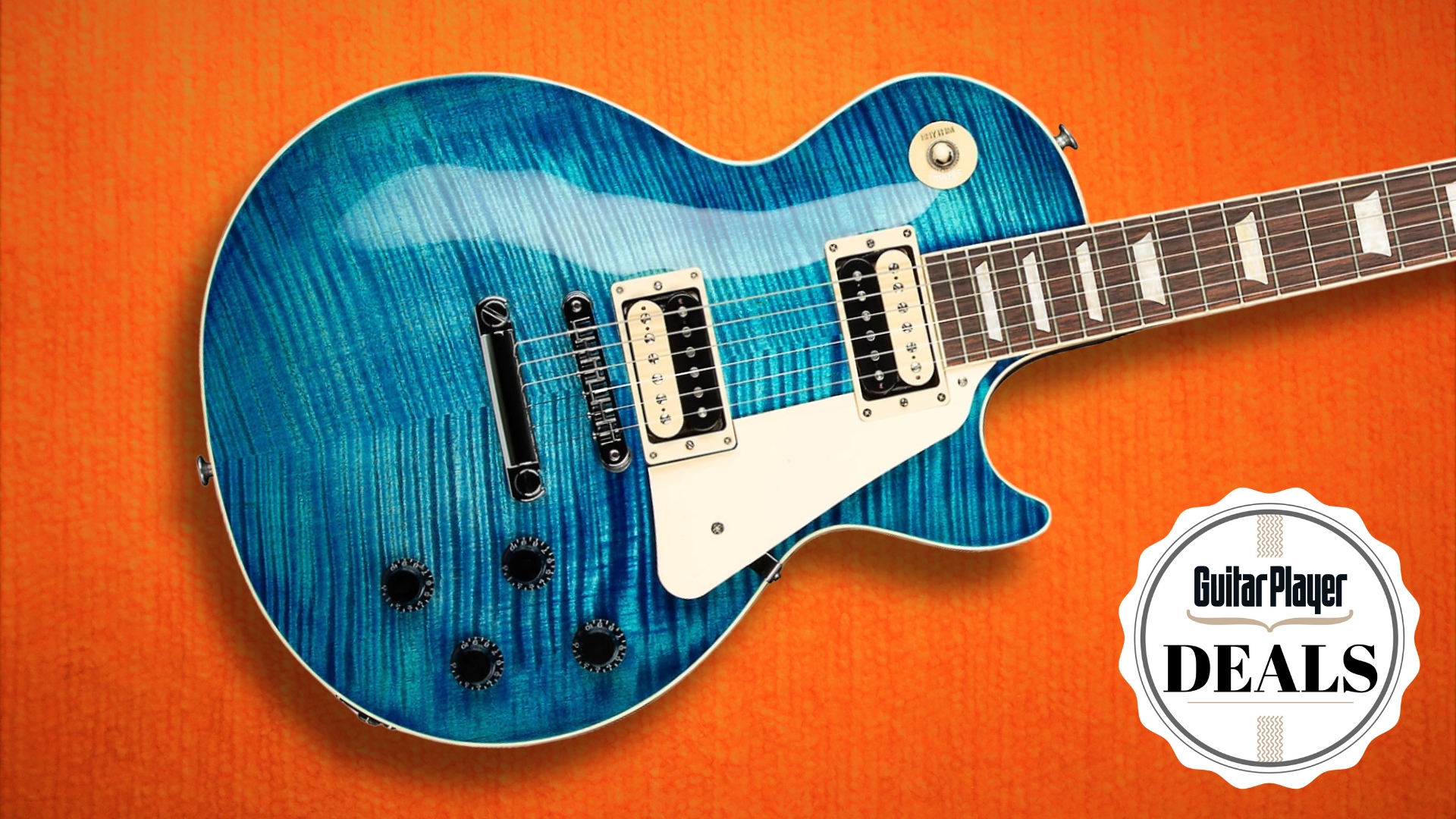A Gibson Les Paul Traditional Pro V electric guitar in Turquoise on textured orange background with the Guitar Player deals logo in the bottom right corner