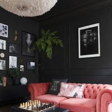 Living room with black walls and ceiling and pink velvet sofa.