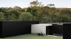 super modern concrete home against the wild backdrop of Australian forests, with a tall black fence surrounding the property