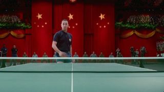 Tom Hanks as Forrest Gump playing ping pong in front of a huge Chinese flag