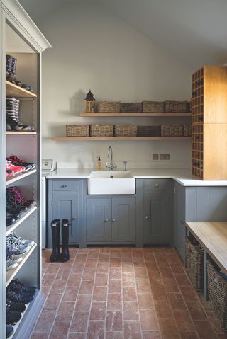 A utility room with blue cabinets, a brickwork floor and clever shelving for footwear