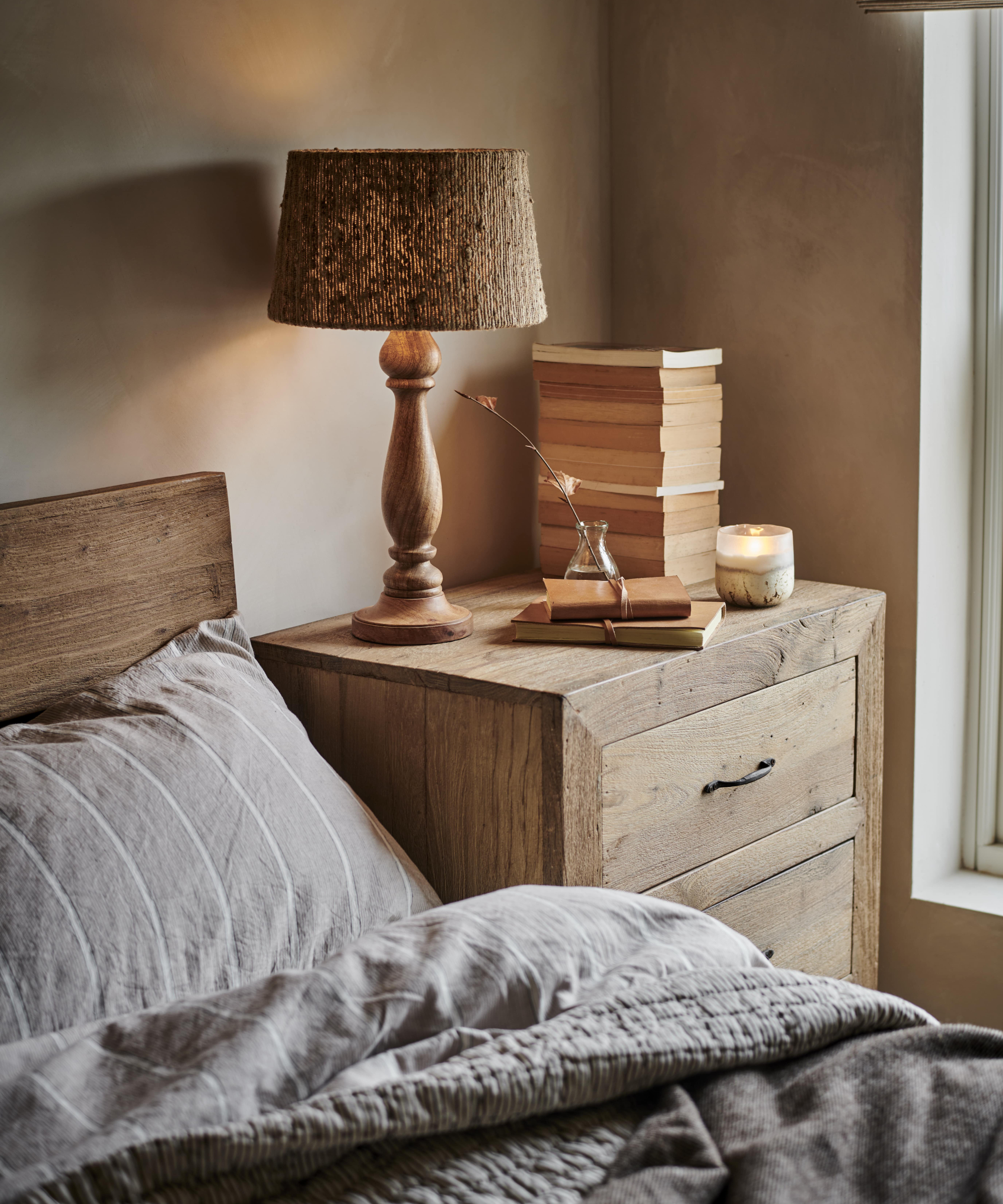 small bedroom with wooden bedside table, table lamp with wooden turned base and fabric shade casting warm light