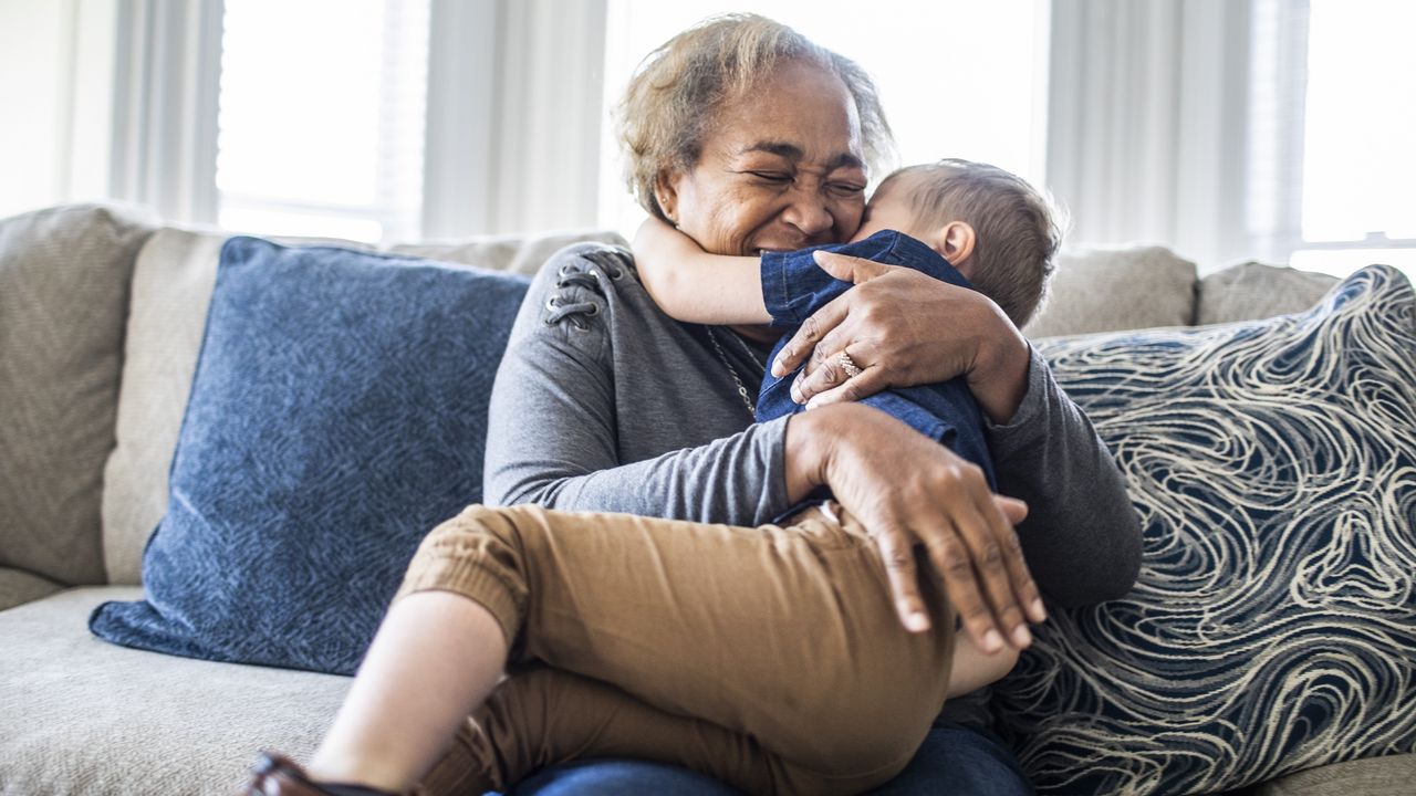 A grandma hugs her grandkid on the sofa.