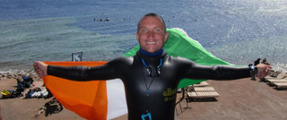 Stephen Keenan in a wetsuit holding an Irish flag