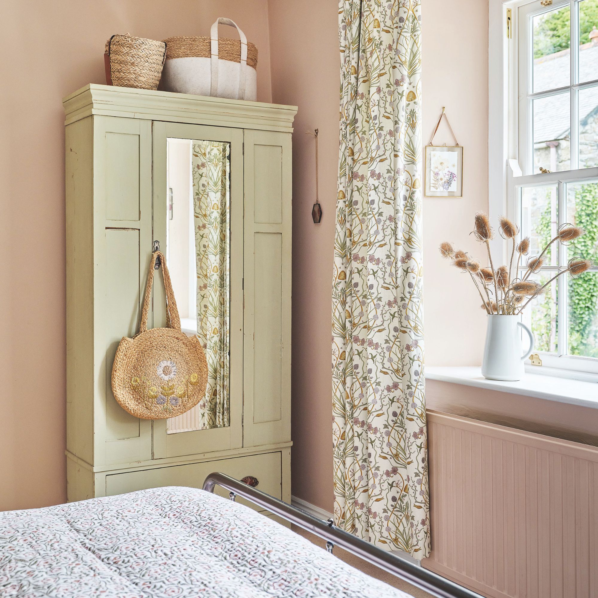 Pink painted bedroom with a cream painted wooden wardrobe in the corner and floral curtains