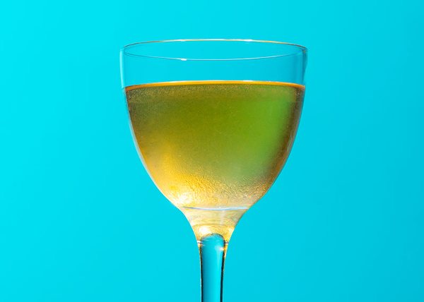 a golden drink in a Nick and Nora glass against a sky-blue background