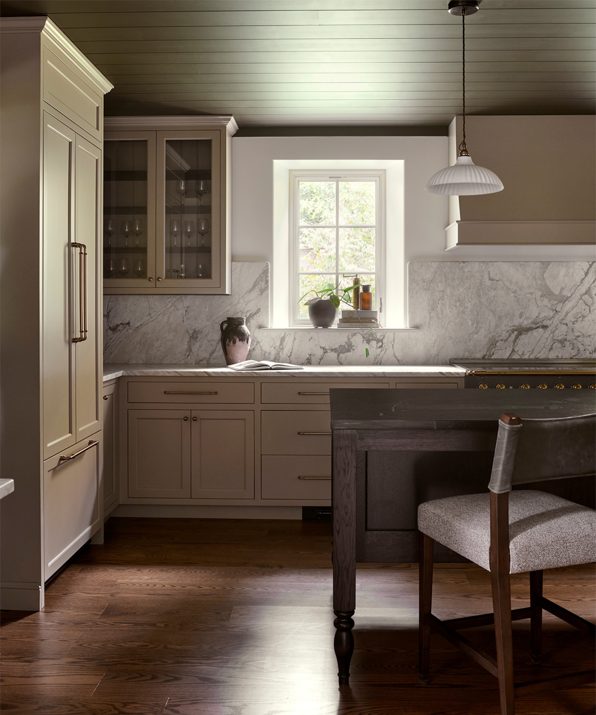 A large kitchen with taupe cabinets, marble countertops, and a wooden island