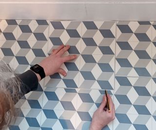 Patterned vinyl tiles with hands holding pencil marking cut