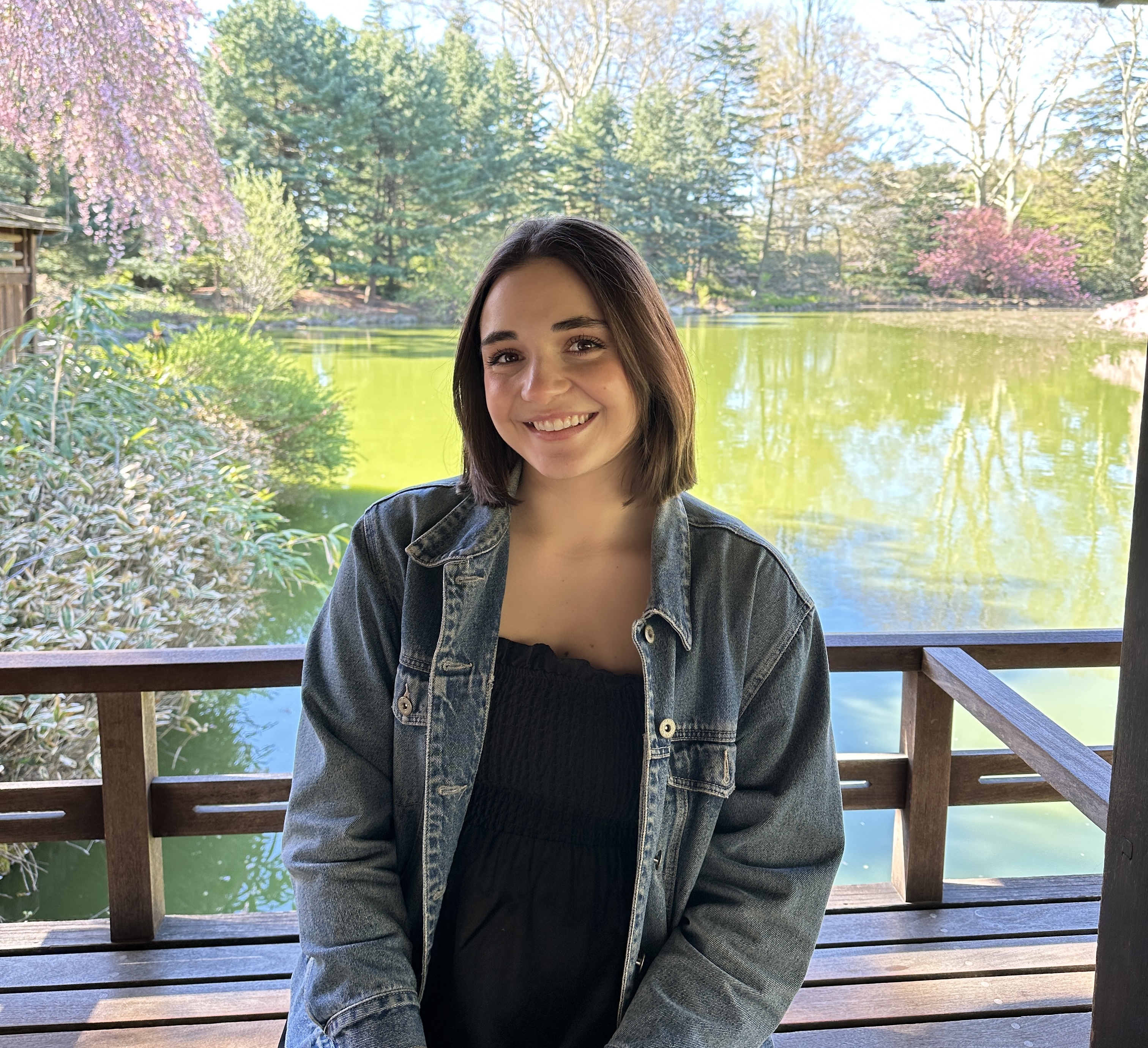 a photo of a woman sitting on a bench in front of a pond in the springtime.