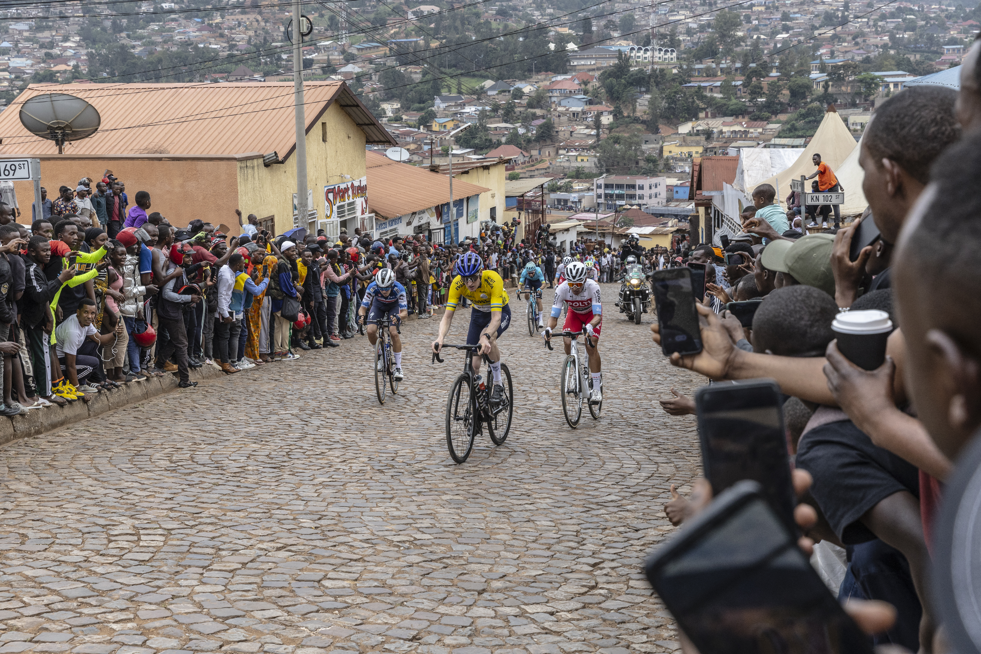 Residents gather to look at Israel Premier Tech&amp;acirc;&amp;#128;&amp;#153;s British rider Joseph Blackmore (C), competing during the final stage of the 16h Tour du Rwanda on 25 February 2024, in Kigali. Blackmore, won the Tour of Rwanda which ended on Sunday in the capital Kigali. (Photo by Guillem Sartorio / AFP)