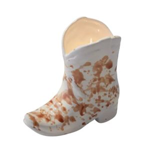 A small, white and brown speckled cowboy boot-shaped candle vessel