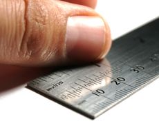 A man's thumb rests on a ruler.