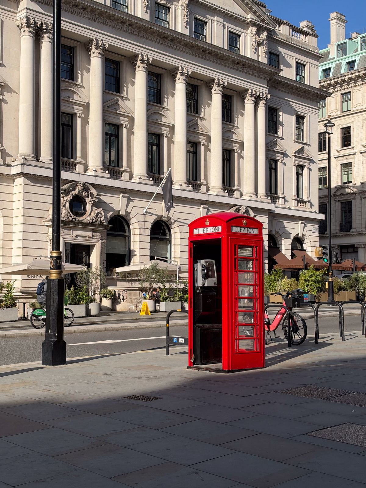 Traditional red British telephone box standing on a London street in front of an ornate stone building.