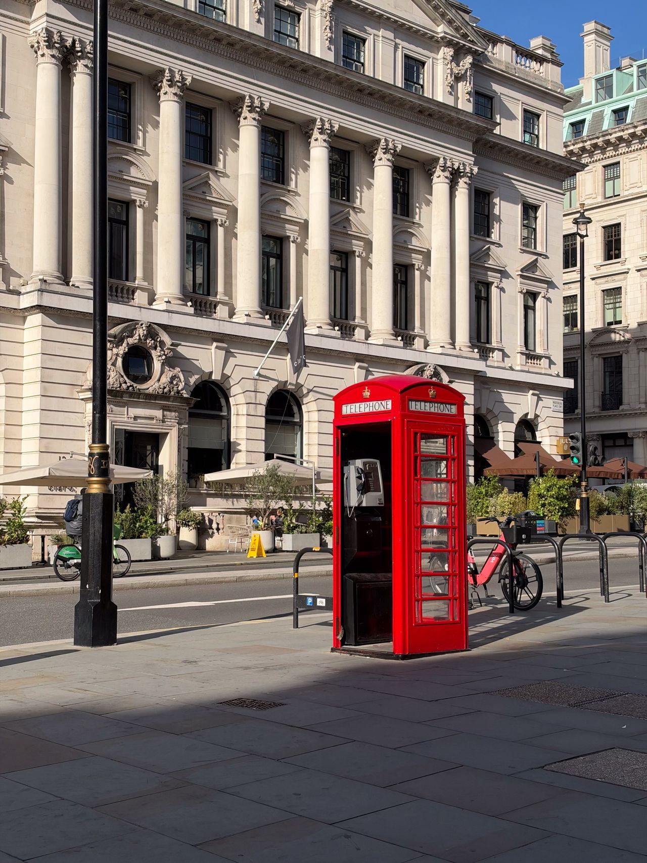 Traditional red British telephone box standing on a London street in front of an ornate stone building.